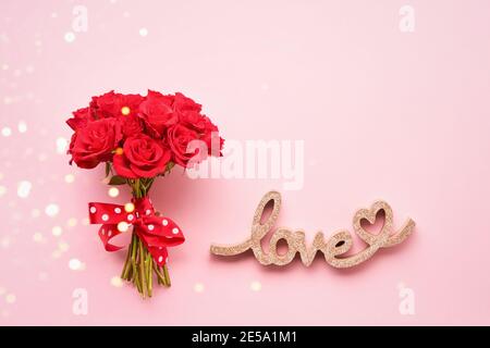 Strauß von roten Rosen Blumen und Wort LIEBE auf einem rosa Hintergrund. Flach liegend, Kopierplatz Stockfoto