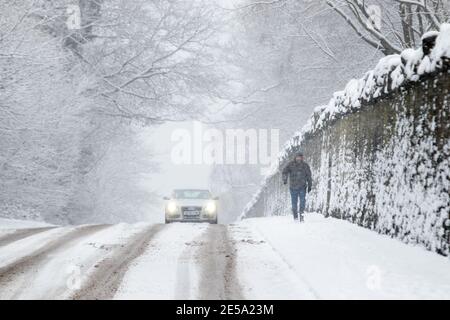 Ein Mann geht entlang der Coleshill Road in der Nähe von Atherstone, als schwerer Schnee auf ihn fällt. Stockfoto