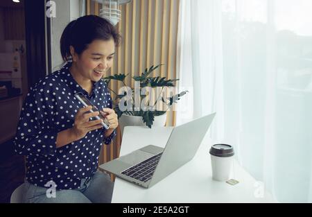 Geschäftsfrau mit Telefonkonferenz über Laptop und Telefon. Heimbüro. Bleiben Sie zu Hause und arbeiten Sie von zu Hause aus während der Coronavirus-Pandemie. Stockfoto