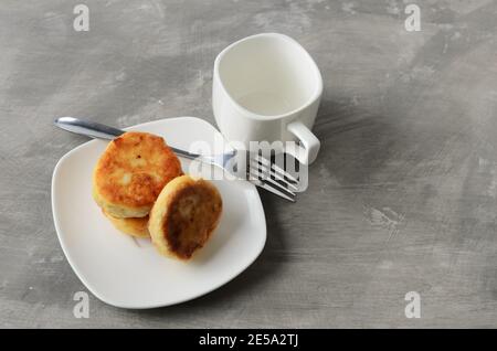 Ein paar Pfannkuchen auf einem weißen Teller mit einer Gabel und einem leeren Becher auf einem texturierten grauen Hintergrund. Selektiver Fokus. Stockfoto