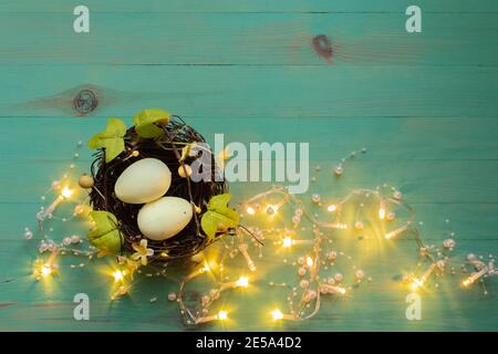 Eier in kleinen Nest von braunen Ästen und grünen Blättern mit gelben Lichtern Girlande um auf vintage grün bemalten Holz Hintergrund. Ostern rustikale Dekora Stockfoto
