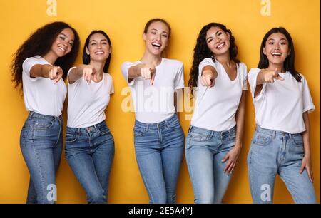 Fröhliche Multiethnische Damen Zeigen Finger Auf Kamera Posiert, Gelber Hintergrund Stockfoto