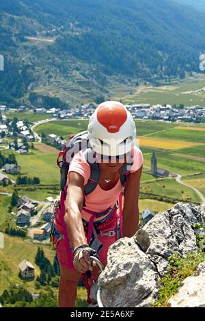 Alte Frau am Klettersteig leicht über das Dorf, Kirche Sainte Cecile im Hintergrund, Frankreich, Hautes Alpes, Ceillac Stockfoto