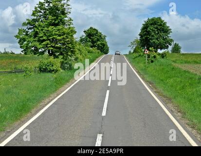 Vorderansicht einer geraden Straße in der Steigung, mit einem Auto in der Ferne Stockfoto