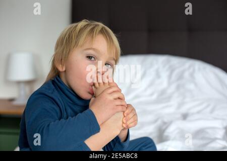 Cute blonde Kleinkind Kind, Saugen seinen Fuß Daumen, macht lustige Gesichter, lachen Stockfoto