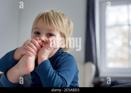 Cute blonde Kleinkind Kind, Saugen seinen Fuß Daumen, macht lustige Gesichter, lachen Stockfoto