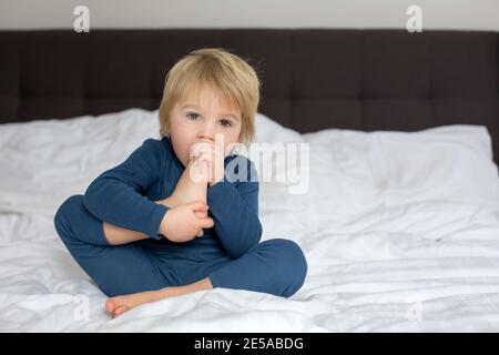 Cute blonde Kleinkind Kind, Saugen seinen Fuß Daumen, macht lustige Gesichter, lachen Stockfoto