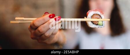 Selektiver Fokus einer Frau, die Sushi mit Essstäbchen hält Stockfoto