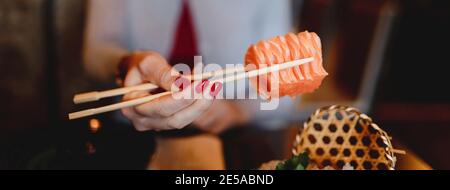Selektiver Fokus einer Frau, die Sushi mit Essstäbchen hält Stockfoto