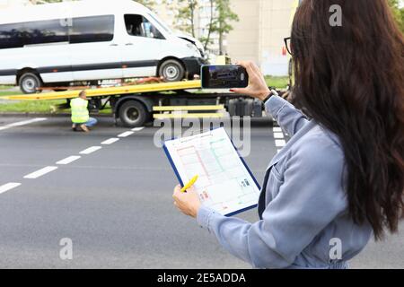 Frau mit Dokumenten in den Händen, die Fotos von zerstörten Auto Am Telefon Stockfoto