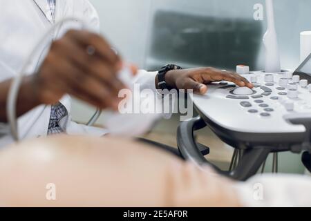 Gesundheitswesen, Ultraschallkonzept. Nahaufnahme eines zugeschnittenen Hands eines afrikanischen Arztes, Screening einer schwangeren Frau durch Ultraschalluntersuchung, Drücken von Tasten Stockfoto