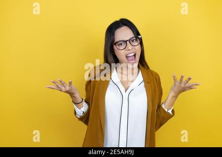 Junge schöne Frau trägt einen Blazer über isolierten gelben Hintergrund verrückt und verrückt schreien und schreien mit aggressivem Ausdruck und Arme angehoben. Stockfoto
