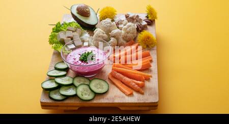 Köstliche bunte Teller voller rohem Gemüse, Avocado, Tofu und rosa Rüben Dip mit Löwenzahn Blumen geschmückt. Stockfoto