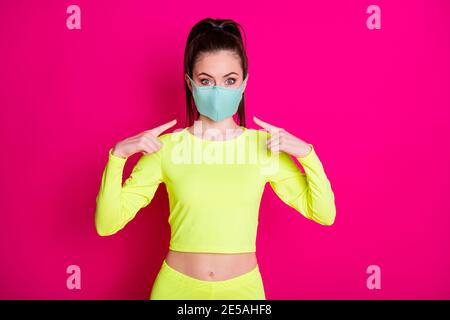 Portrait Foto von Mädchen zeigt auf medizinische Schutzmaske tragen Sportswear Pferdeschwanz isoliert auf lebendige fuchsia Farbe Hintergrund Stockfoto