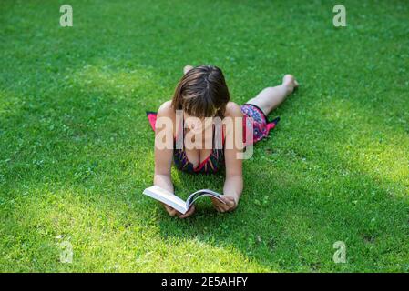 Junge Frau, die im grünen Gras liegt und ein Buch liest. Stockfoto