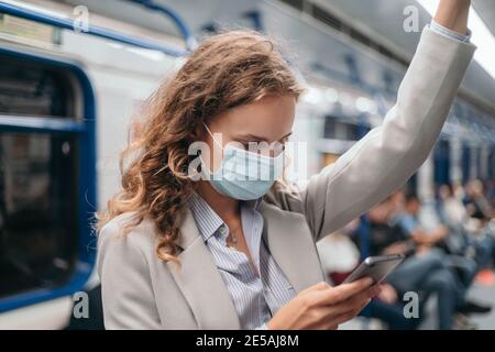 Junge Frau in einer Schutzmaske, die auf einer U-Bahn steht. Stockfoto