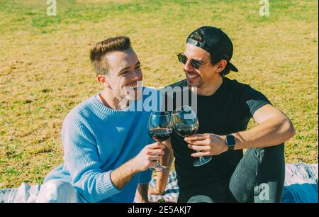 Schöne junge Erwachsene kaukasischen Homosexuell Paar lachen, Blick auf einander und trinken Rotwein Stockfoto