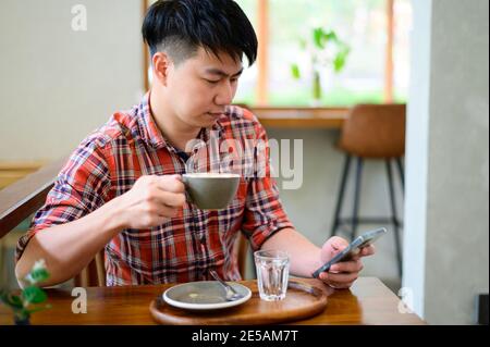 Junge asiatische Mann mit Smartphone und Kaffee Stockfoto