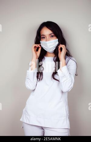 Junge asiatische Frau Arzt in weißen Uniform gestikulieren positiv auf grauem Hintergrund, das Tragen einer Maske, Lifestyle Gesundheit Menschen Konzept Stockfoto