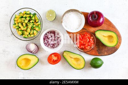 Avocado Hälften, Stücke, Limetten, Tomaten und Zwiebeln, Tasse mit Salz - Grundzutaten Guacamole auf weißem Arbeitsbrett, flach legen Foto. Stockfoto