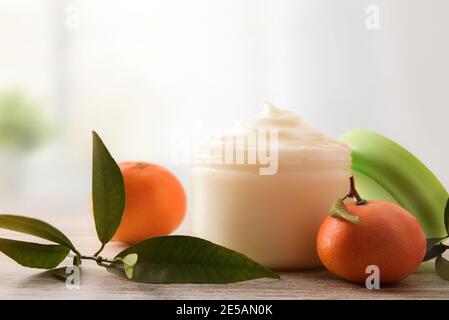 Natürliche Hautcreme mit Mandarinenextrakt mit Früchten und Blättern auf Holztisch. Vorderansicht. Stockfoto