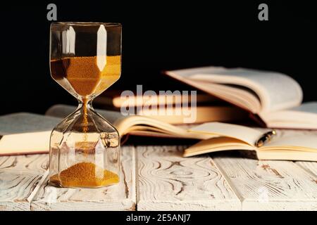 Sandglas auf Holztisch mit geöffnetem Buch aus nächster Nähe Stockfoto