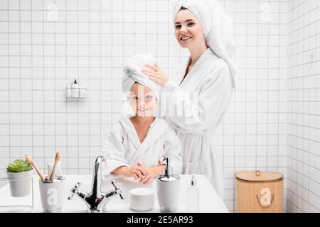 Fröhliche Mutter und Kind mit Handtüchern auf den Köpfen Blick auf Kamera im Badezimmer Stockfoto