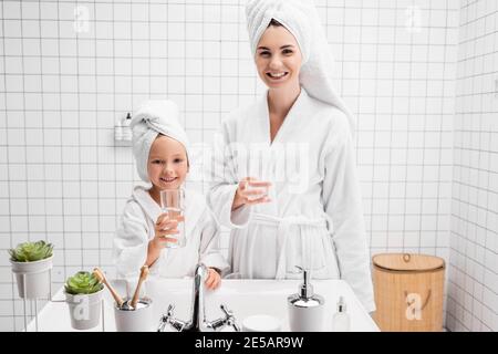 Positive Mutter und Tochter halten Gläser Wasser im Badezimmer Stockfoto