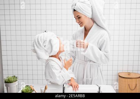 Mutter und Tochter halten Gläser Wasser im modernen Badezimmer Stockfoto