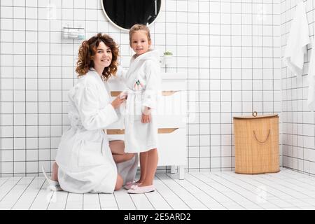 Mutter und Tochter in Bademänteln lächeln im Badezimmer vor der Kamera Stockfoto