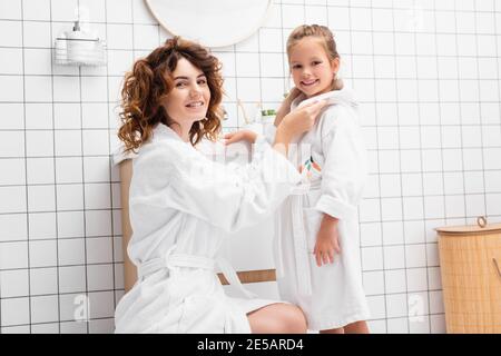 Fröhliche Mutter und Kind in Bademänteln, die in die Kamera schauen Badezimmer Stockfoto