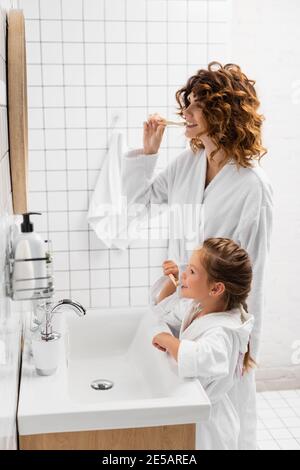 Mutter und Tochter in Bademänteln putzten die Zähne neben dem Spiegel Stockfoto
