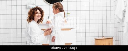 Lächelnde Frau trägt Bademantel auf Tochter im Badezimmer, Banner Stockfoto