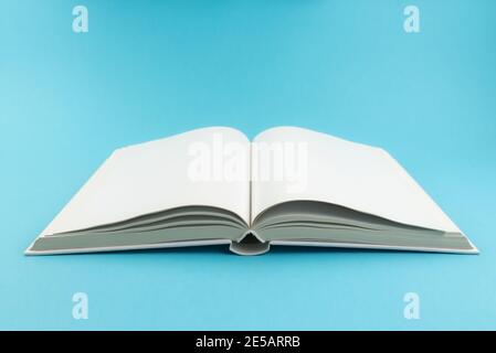 Öffnen Sie ein Hardcover-Buch mit leeren weißen Seiten auf blauem Hintergrund Stockfoto