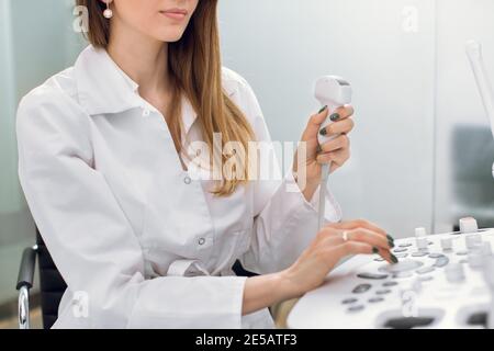 Nahaufnahme eines zugeschnittenen Porträts einer professionellen Ärztin, die ein modernes Ultraschallgerät bei der Arbeit verwendet und Ultraschall in der Hand hält Stockfoto