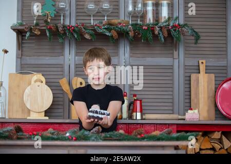 Ein Junge in der Weihnachtsküche zu Hause hält einen Kuchen in den Händen. Stockfoto