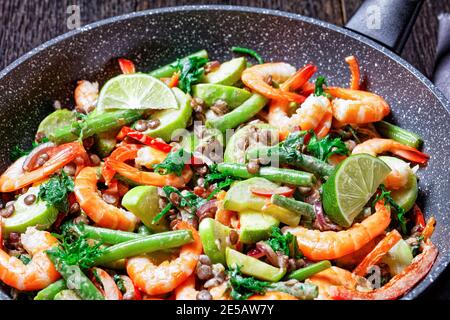 Warmer mediterraner Salat aus Linsen, grünen Bohnen, Paprika, Garnelen mit wildem Grünkohl, mit Limette und Tahini-Sauce auf einer Pfanne serviert Stockfoto