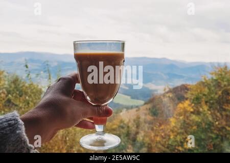 Frau hält ein Glas mit Chai Latte mit Aussicht In die Berge Stockfoto