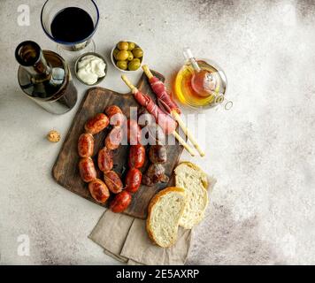 Spanische Bratwürste auf dem Schneidebrett - butifarra blanca, Chorizo, morcilla de cebolla, Jamon und Knoblauch aus aioli Stockfoto