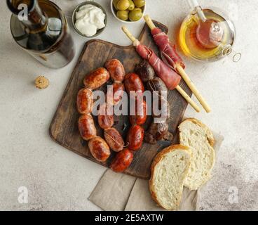 Spanische Bratwürste auf dem Schneidebrett - butifarra blanca, Chorizo, morcilla de cebolla, Jamon und Knoblauch aus aioli Stockfoto