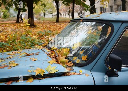 Gelbe Blätter auf dem alten Retro-Auto. Vintage kaputtes Auto unter Bäumen im Park in der Herbstsaison. Charkiw, Ukraine Stockfoto