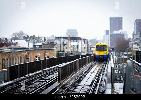 Ein Overground Zug nähert sich Haggerston Station an einem kalten verschneiten Tag. Stockfoto