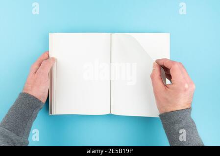 Direkt über Ansicht der Person, die Seite von blank weiß dreht Seite Hardcover Buch auf blauem Hintergrund Stockfoto