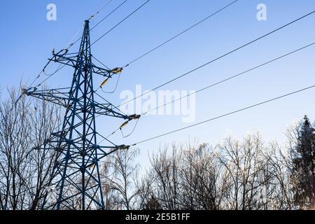 Stahlübertragungsturm der Hochspannungsleitung und Sonnenbeleuchtung eisgekühlte Gipfel von gefrorenen Bäumen im Stadtpark auf kalt Wintertag Stockfoto