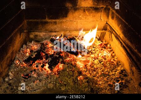 Schwelendes Feuerholz und heiße Asche im Kamin Stockfoto