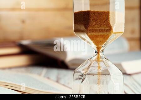Sandglas auf Holztisch mit geöffnetem Buch aus nächster Nähe Stockfoto