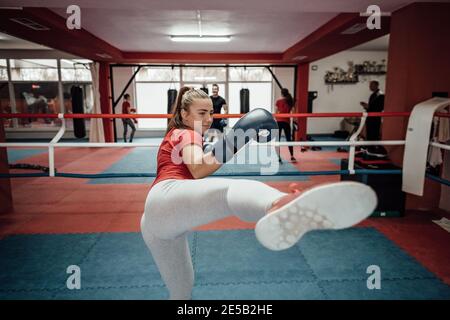 Nahaufnahme einer jungen weiblichen Boxerin mit Boxhandschuhen, die in Richtung einer Kamera treten. Ein Mädchen in einer Kickboxen-Klasse. Stockfoto