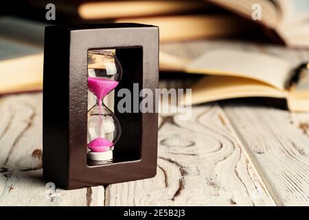 Sandglas auf Holztisch mit geöffnetem Buch aus nächster Nähe Stockfoto