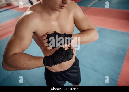 Zugeschnittenes Bild eines jungen Sportlers, der seine Hände zum Boxen einwickelt. Porträt eines Kickboxers, der seine Handgelenke verband und sich für eine Boxfigur vorbereite Stockfoto