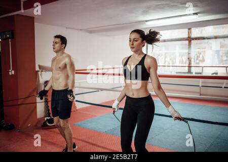 Ein Mann und eine Frau springen zusammen in einem Sportverein. Ein Paar trainiert mit einem Springseil in einer Turnhalle. Stockfoto